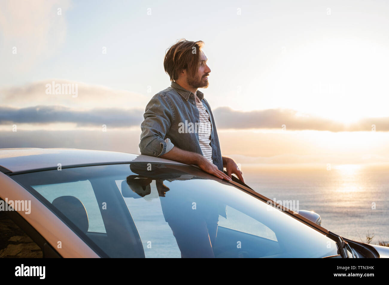 Junge Menschen suchen beim Stehen vor dem Auto mit Meer bei Sonnenuntergang Stockfoto