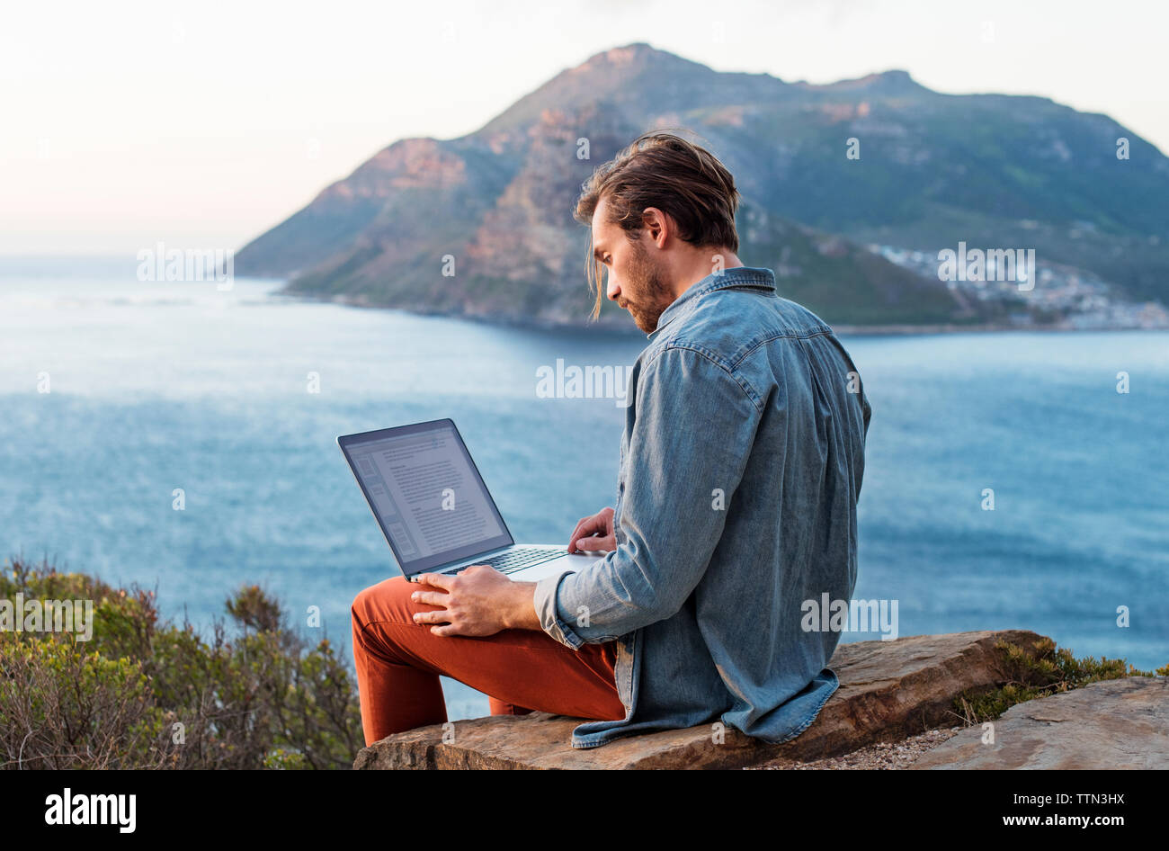 Seitenansicht der Mann mit Laptop auf dem Hügel gegen Berg und Meer Stockfoto