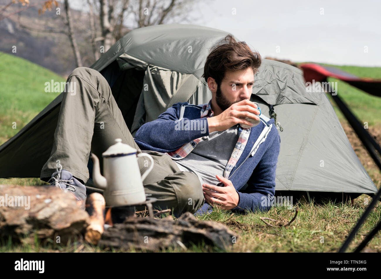 Nachdenklicher Mann trinkt Tee, während sie sich außerhalb der Hütte auf dem Hügel Stockfoto