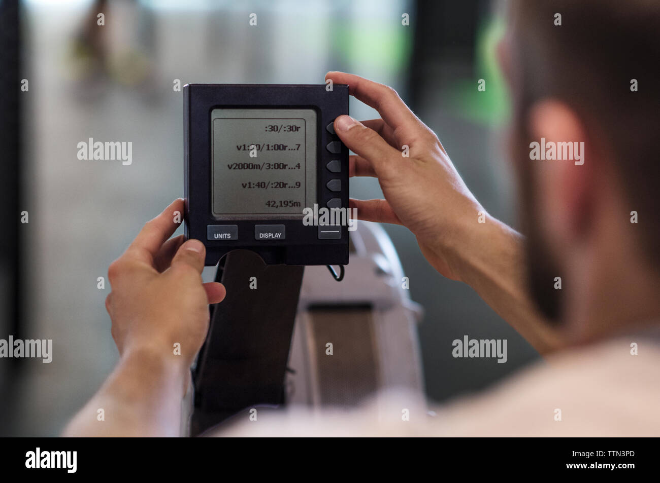 Zugeschnittenes Bild des Athleten mit Monitor am Rudergerät in der Turnhalle Stockfoto