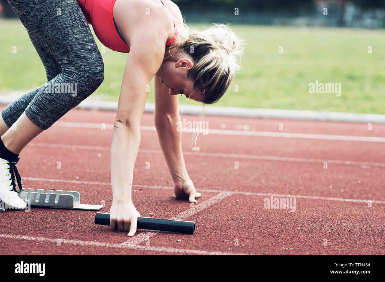 Athlet mit staffelstab am Startblock auf Schiene balanciert Stockfoto