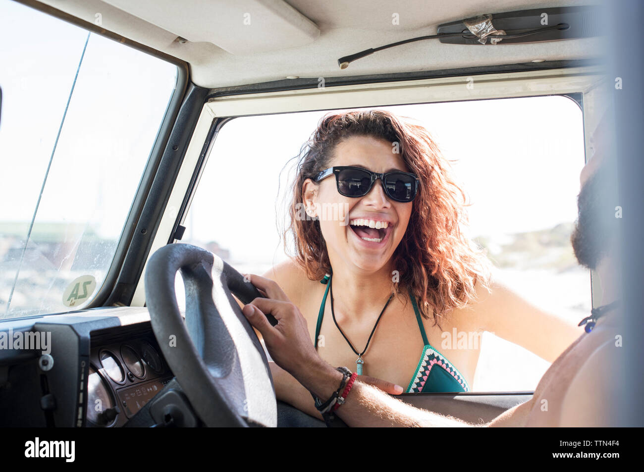 Fröhliche Frau mit Sonnenbrille im Gespräch mit männlichen Freund in Off-road-Fahrzeug sitzen Stockfoto