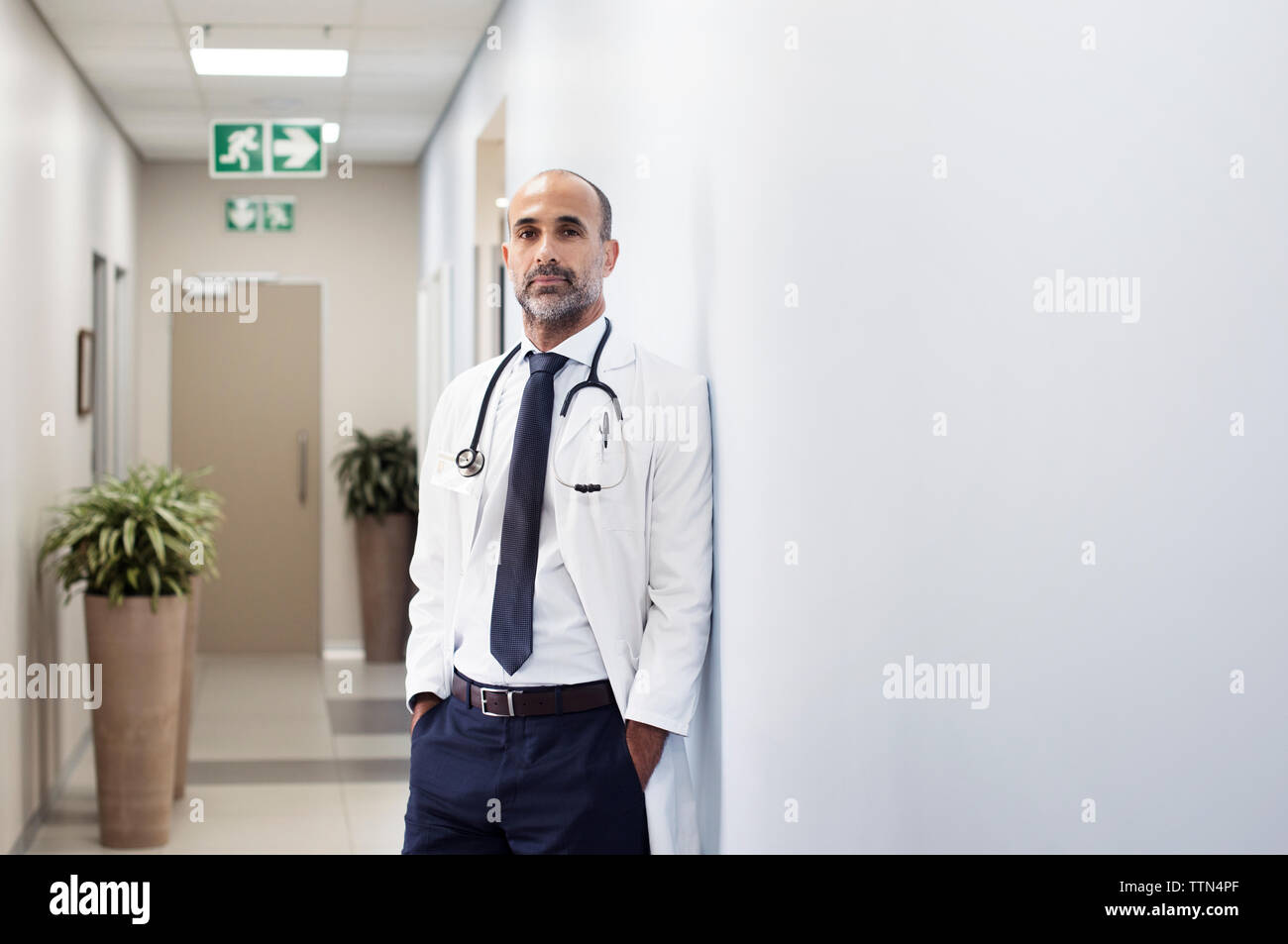 Portrait von Arzt mit Händen in den Taschen an der Wand am Krankenhaus schiefen Stockfoto