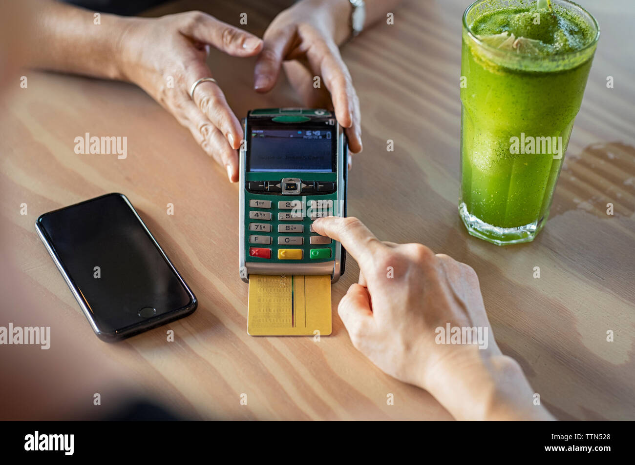 7/8 Hände der weiblichen Kunden die Bezahlung per Kreditkarte an Eigentümer auf hölzernen Tisch in der Cafeteria Stockfoto