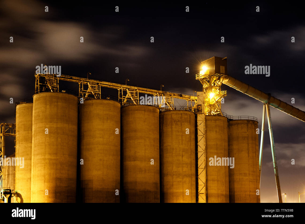 Low Angle Blick auf das beleuchtete Lagertanks an der Industrie gegen bewölkter Himmel Stockfoto