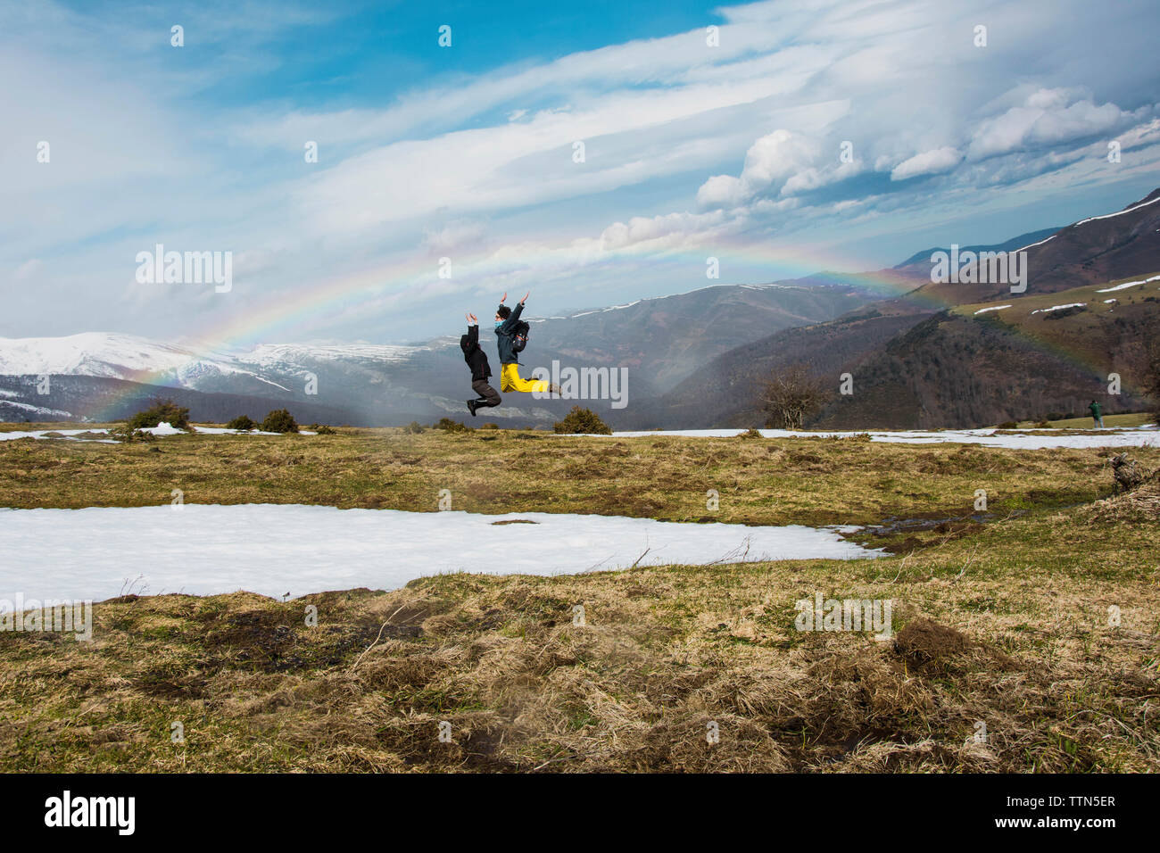 Aufgeregt Freunde springen gegen Berge und Regenbogen im Winter Stockfoto
