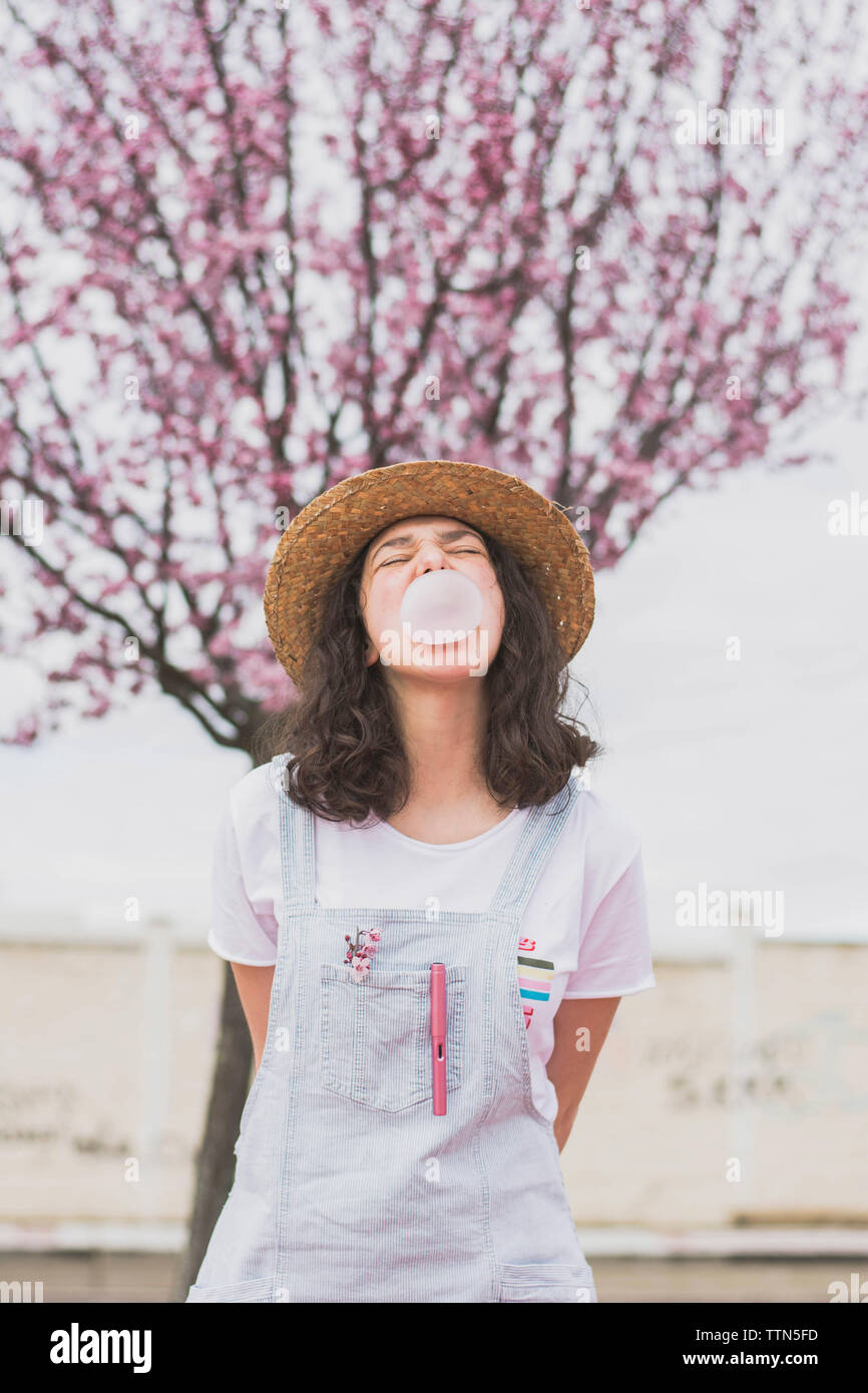 Junge Frau blasen Bubble Gum, während gegen cherry tree in PARK-Stellung Stockfoto