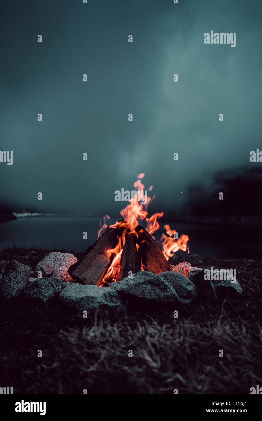 Lagerfeuer auf Feld am Seeufer gegen bewölkter Himmel bei Nacht Stockfoto