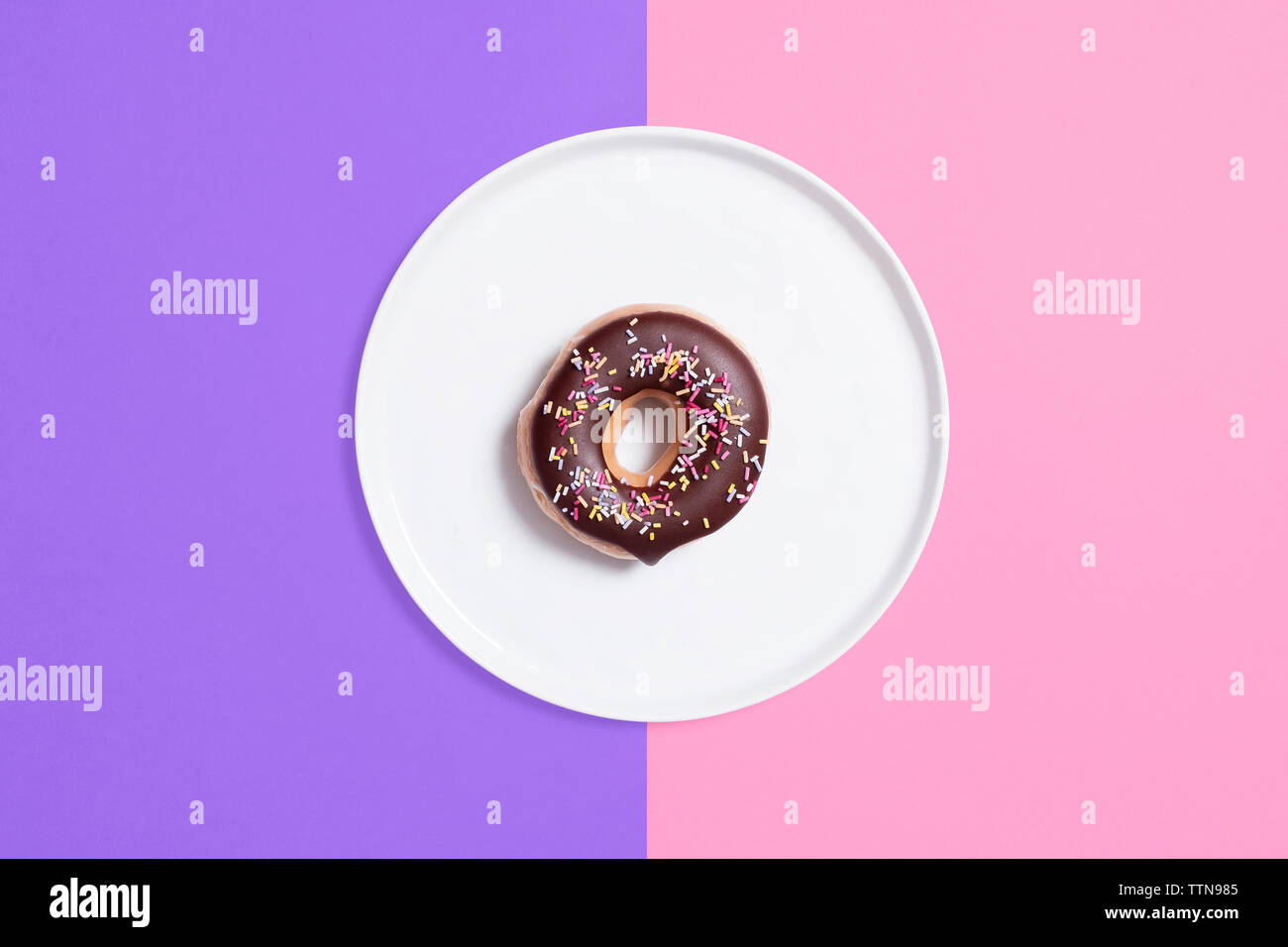 Ansicht von oben der Schokolade Donut mit Streuseln in der Platte auf farbigem Hintergrund Stockfoto