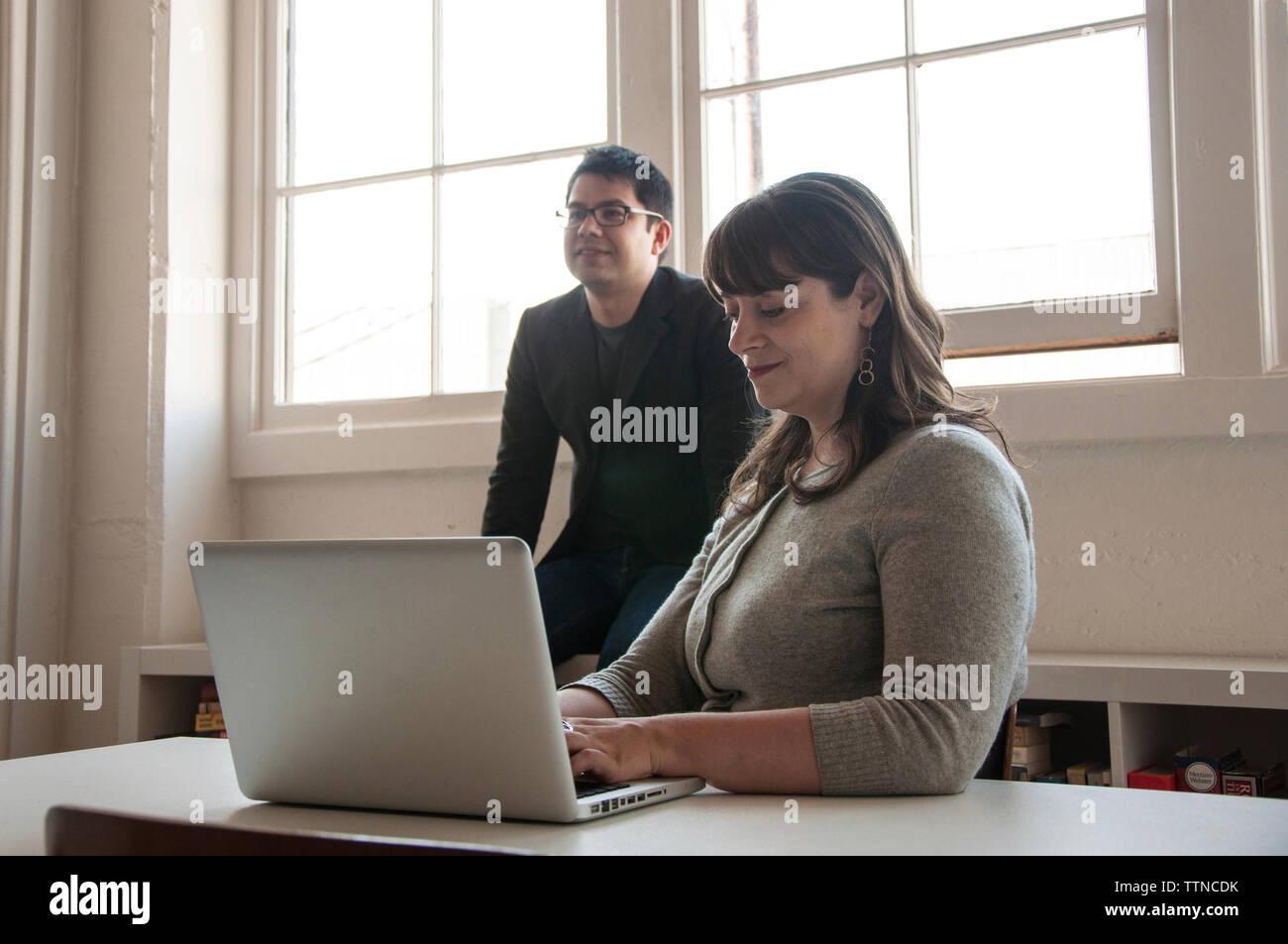 Geschäftsfrau, die einen Laptop benutzt, während Geschäftsmann im Hintergrund im neuen Büro sitzt Stockfoto