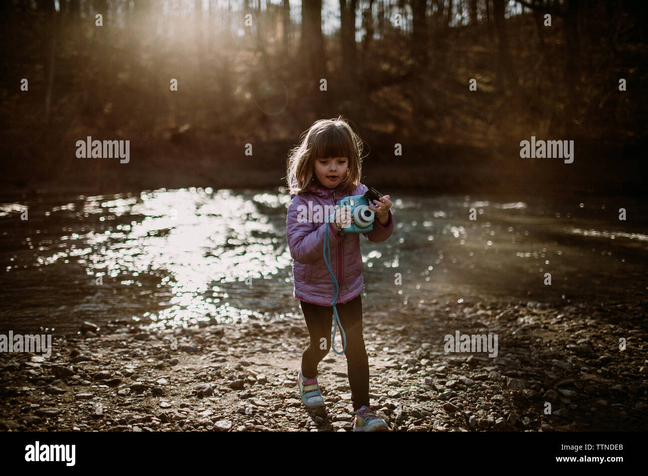 Kleines Mädchen Holding instax Camera durch den Fluss mit Sunflare Stockfoto