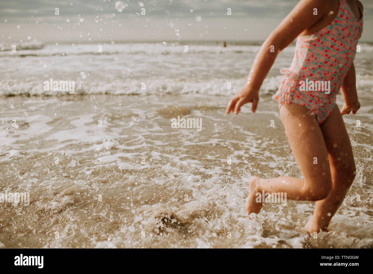 Junge Mädchen tragen Badehose, Spritzwasser durch Ocean Surf, 7/8 Stockfoto