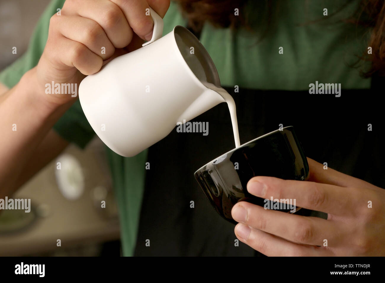 Man gießt Sahne im Kaffee Stockfoto