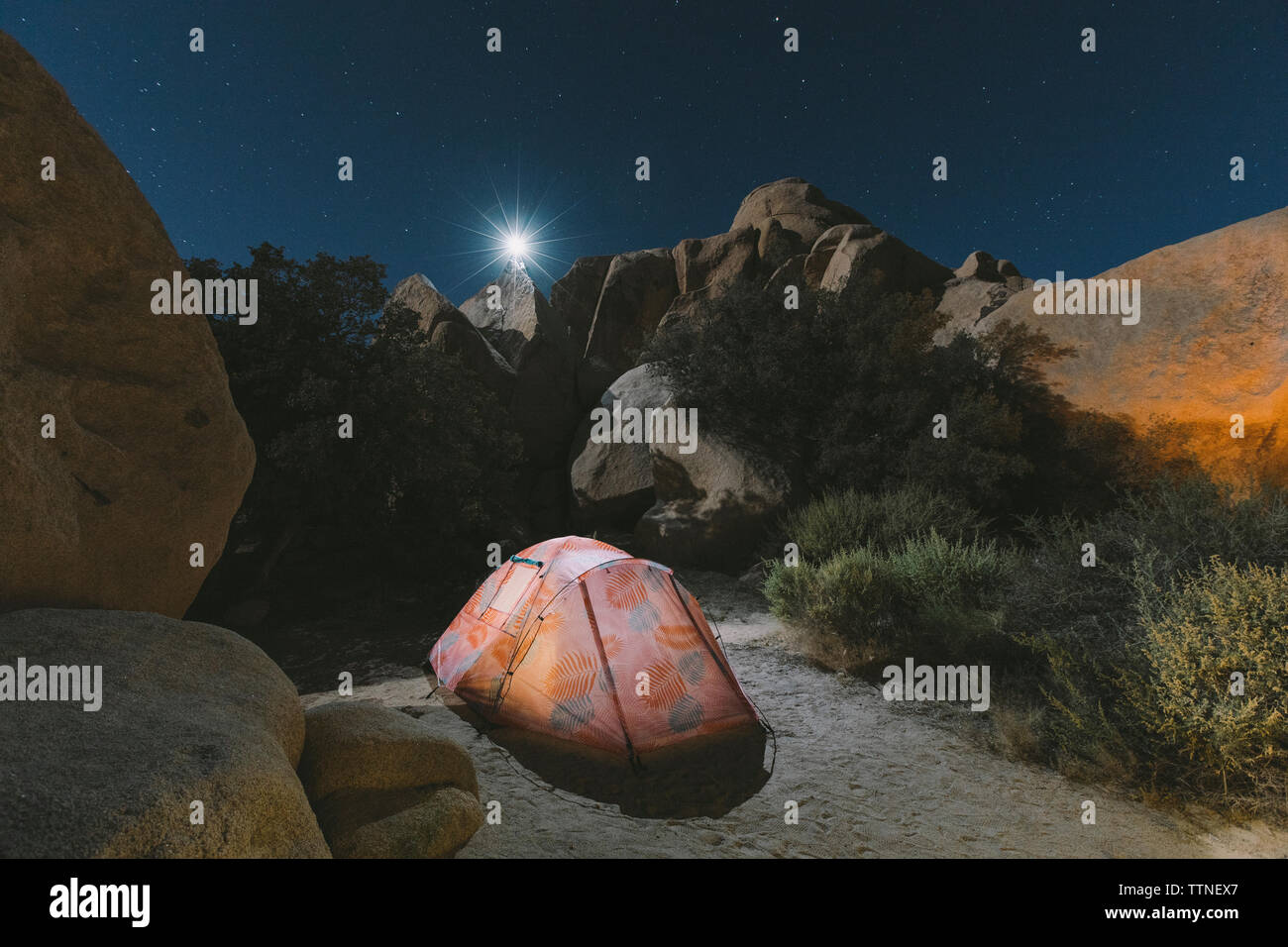 Beleuchtetes Zelt auf Wüste gegen Felsen im Joshua Tree National Park bei Nacht Stockfoto