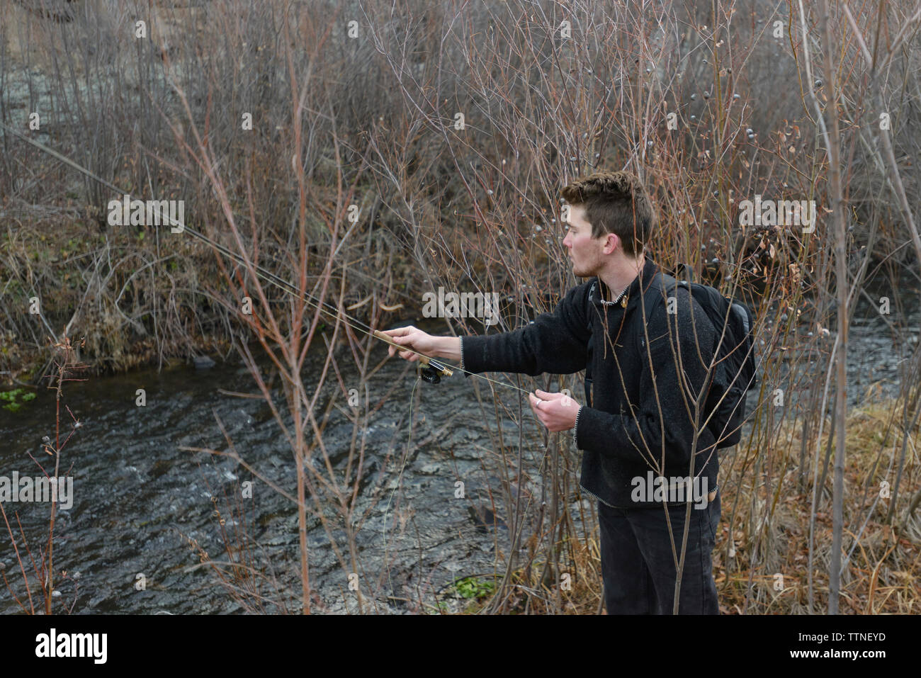 Junger Mann mit Rucksack Angeln im Stream beim stehen inmitten von Pflanzen auf dem Feld Stockfoto