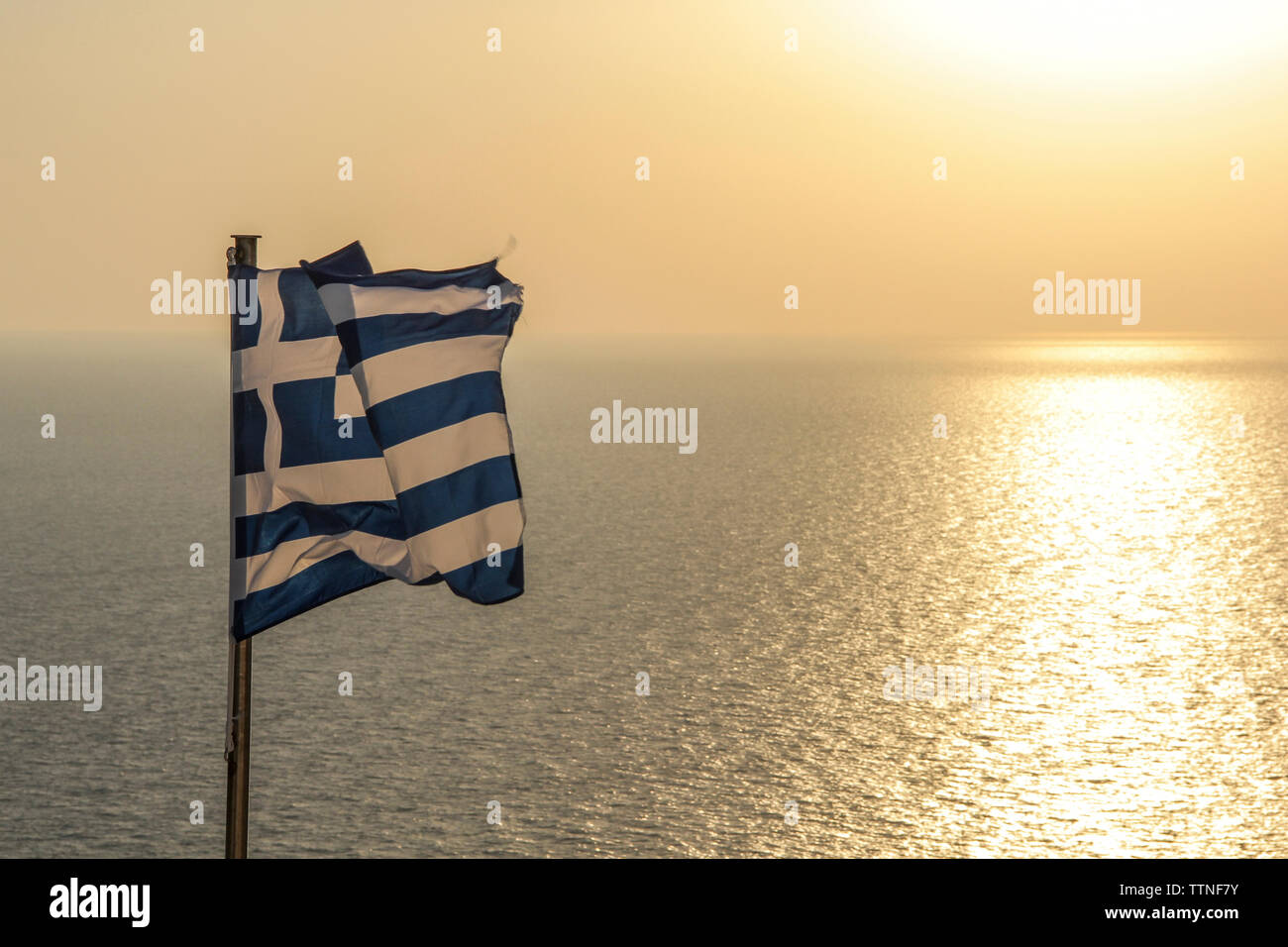 Griechische Flagge schwenkten auf See gegen Himmel bei Sonnenuntergang Stockfoto