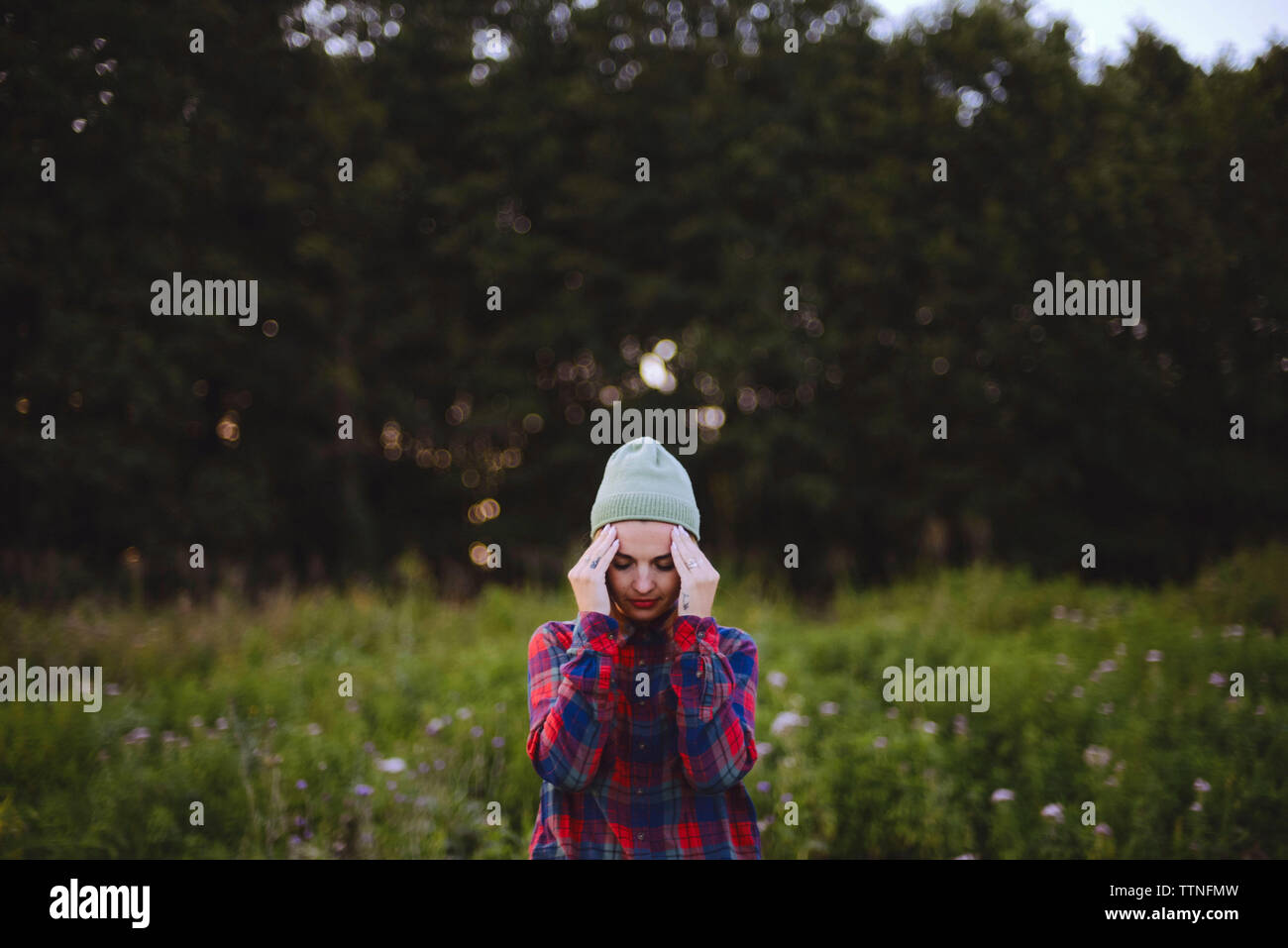 Junge Frau mit Kopf in den Händen stehend auf dem Feld Stockfoto