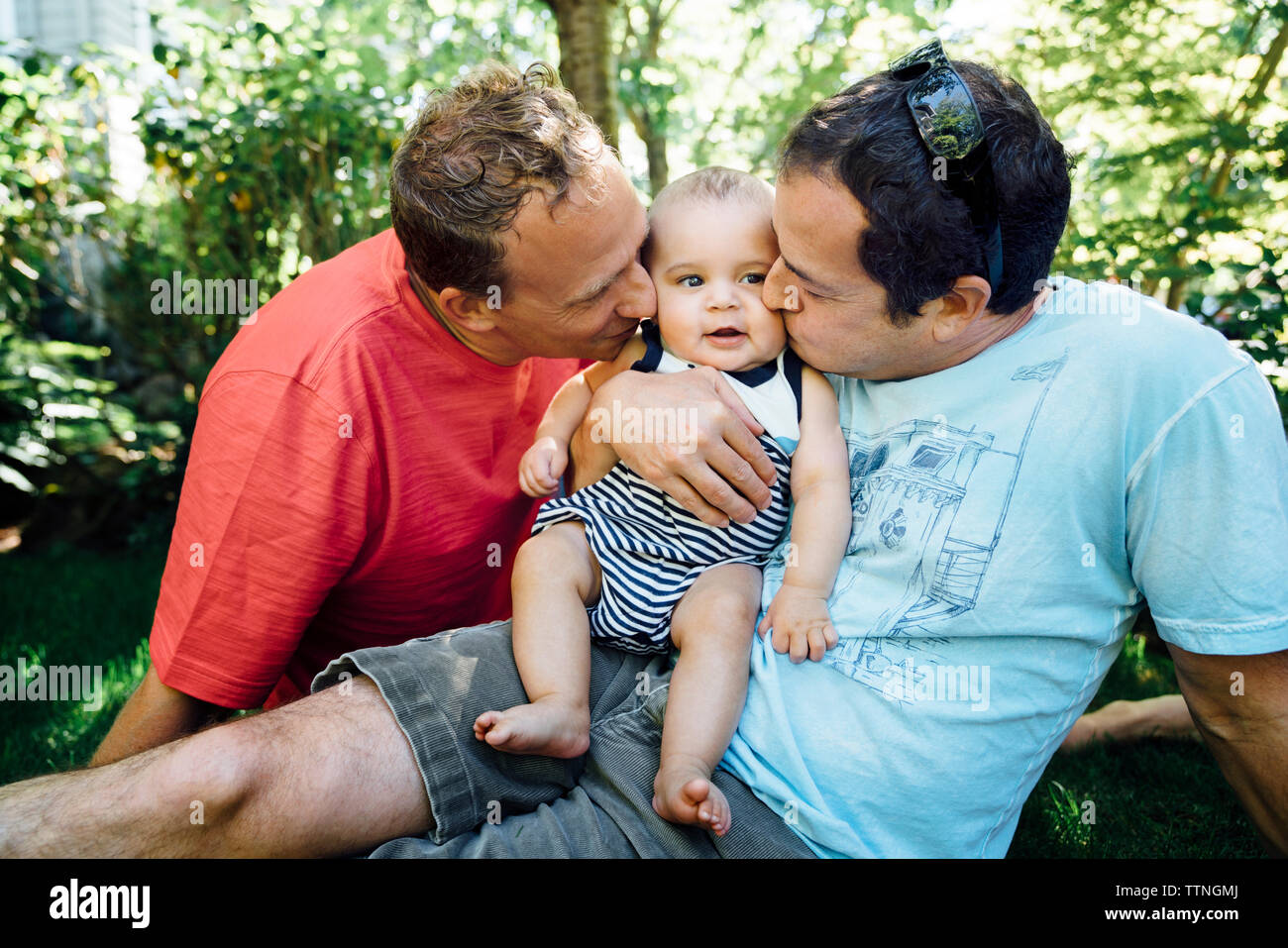 Homosexuelle Paare küssen Baby, während im Hinterhof sitzen Stockfoto