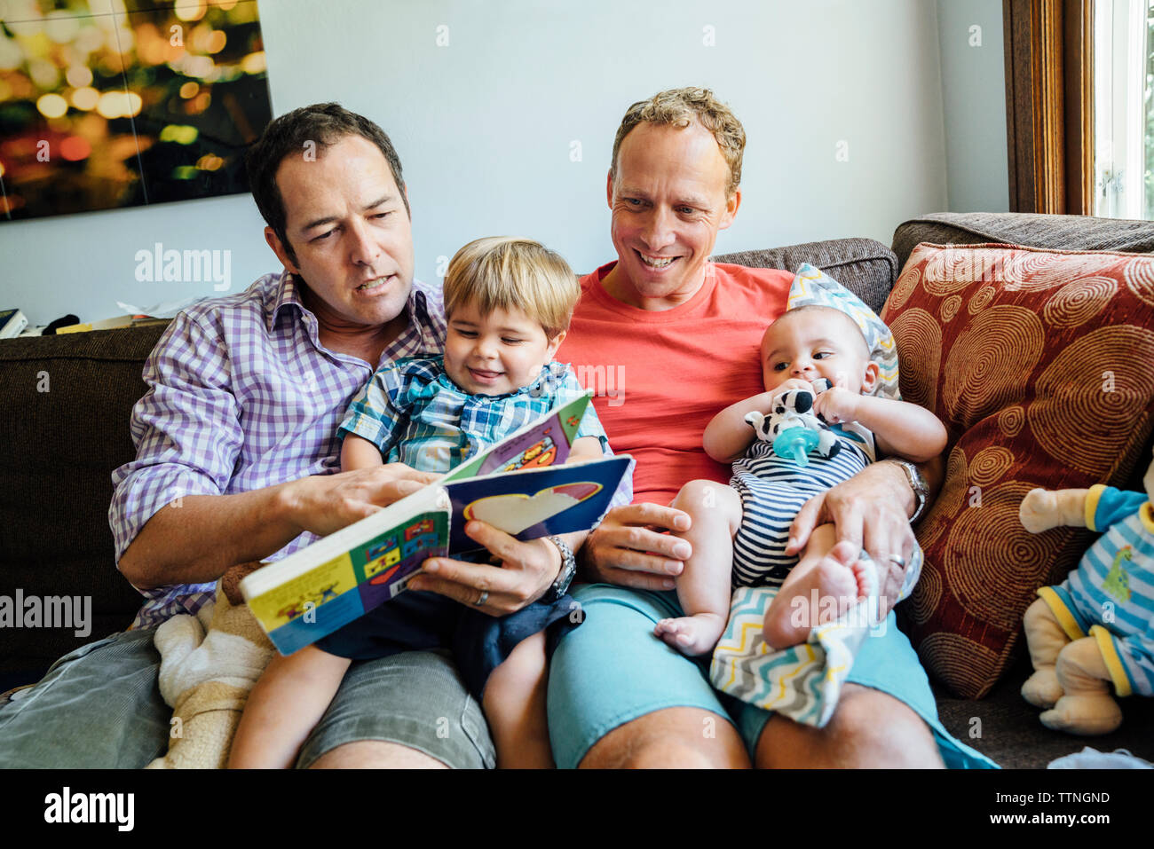 Homosexuelle Paare lesen Buch mit Söhne auf dem Sofa zu Hause Stockfoto