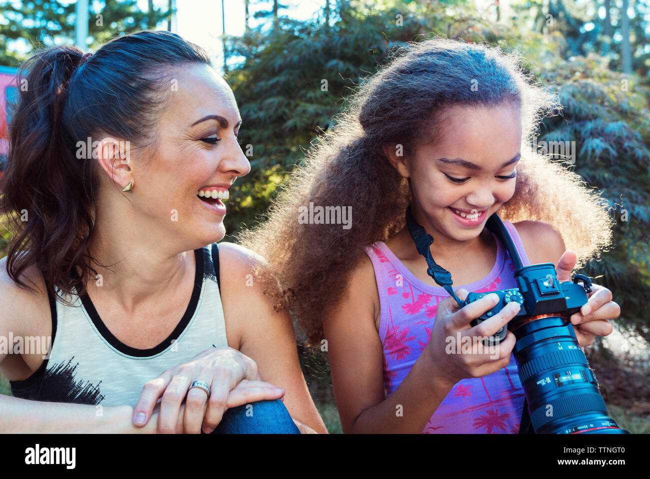 Glückliche Mutter und Tochter auf der Suche nach Digitalkamera während der Sitzung in Hof Stockfoto