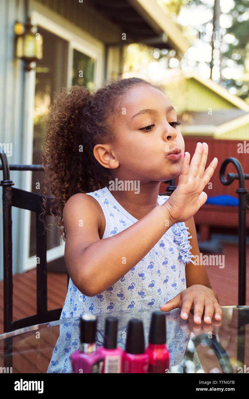 Mädchen bläst Nagellack auf fingernägeln beim Sitzen am Tisch im Hof Stockfoto