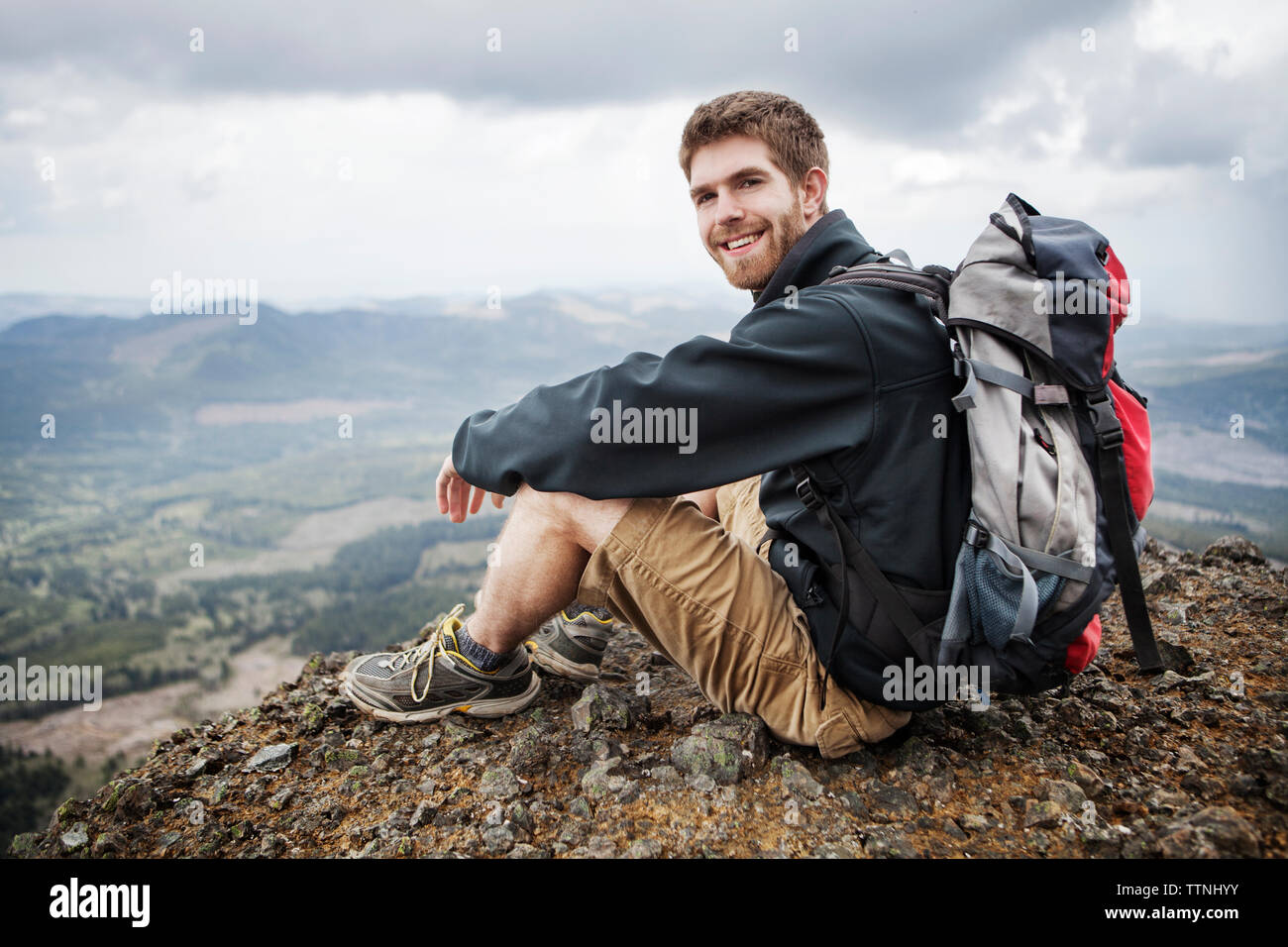 Portrait von lächelnden Mann, der Rucksack beim Sitzen auf dem Berg Stockfoto