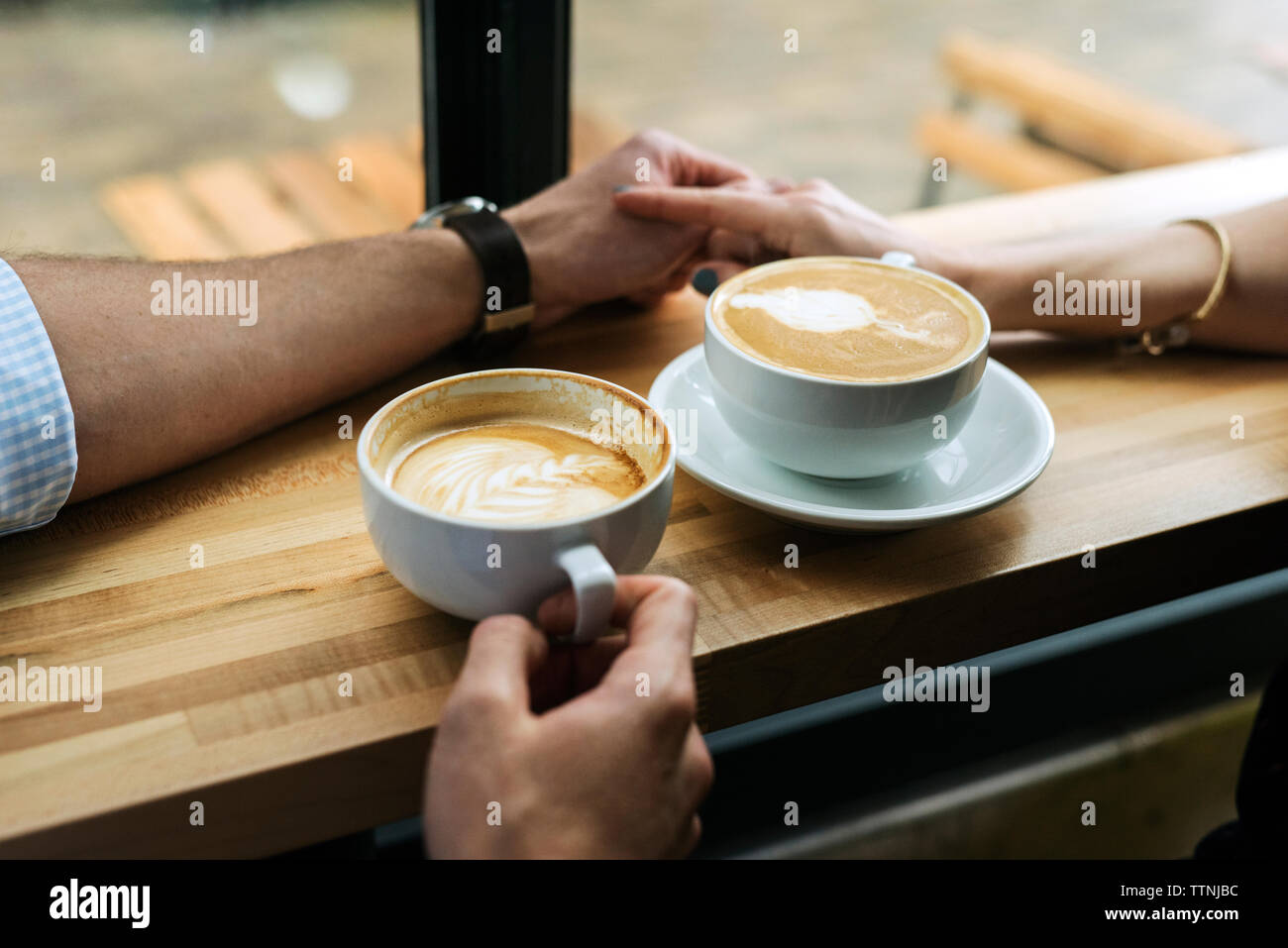 Zugeschnittenes Bild der Paare Hand in Hand durch Kaffee am Tisch im Cafe Stockfoto