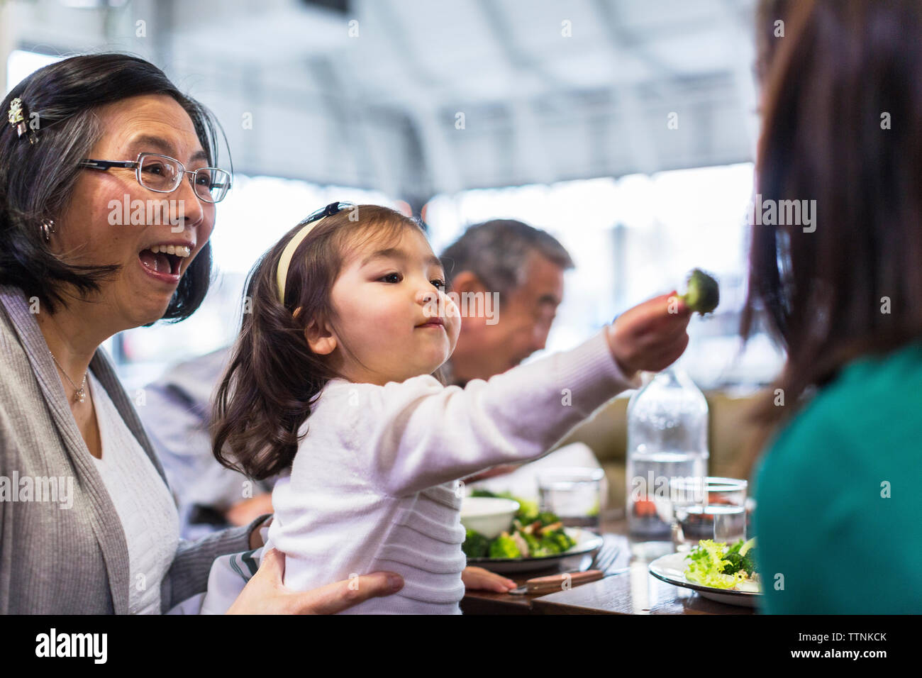 Mädchen Fütterung Mutter während der Sitzung mit den Großeltern am Tisch im Restaurant Stockfoto