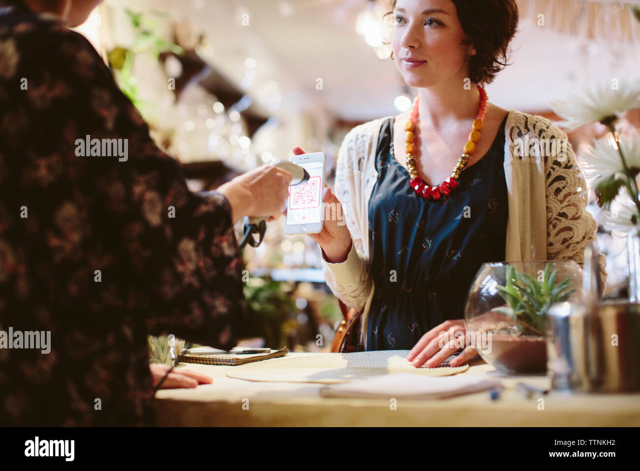 Mittelteil des Eigentümers scannen QR-Code vom Handy Holding, die der Kunde in Pflanzen shop Stockfoto