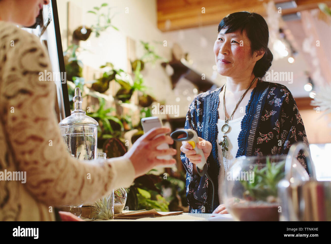 Mittelteil des Kunden holding Handy lächelnd Eigentümer scannen QR-Code in Pflanzen shop Stockfoto