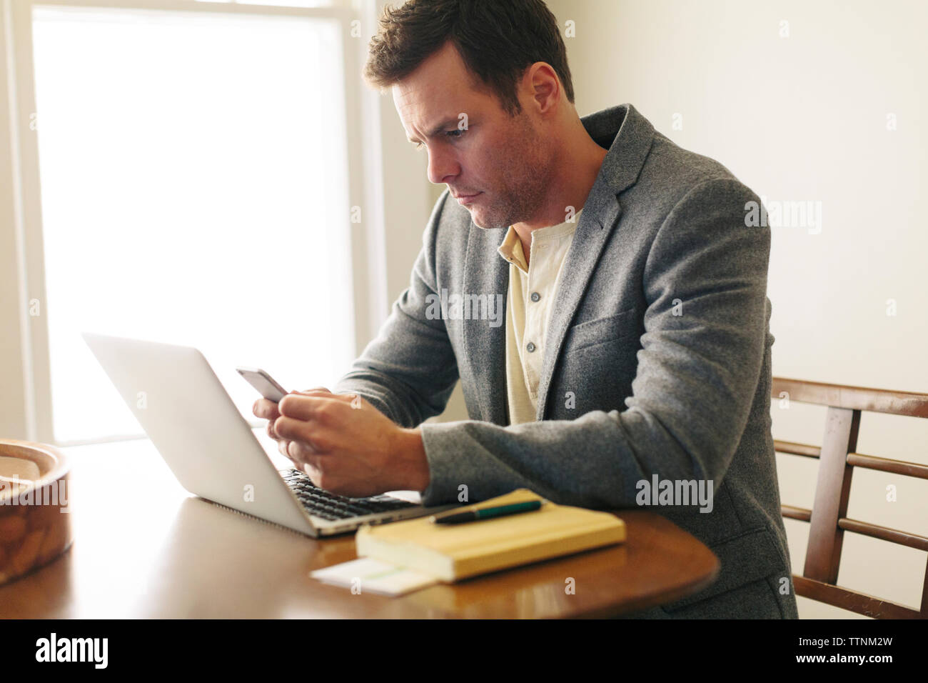 Mann mit Smart Phone, während mit Laptop auf dem Tisch zu Hause sitzen Stockfoto