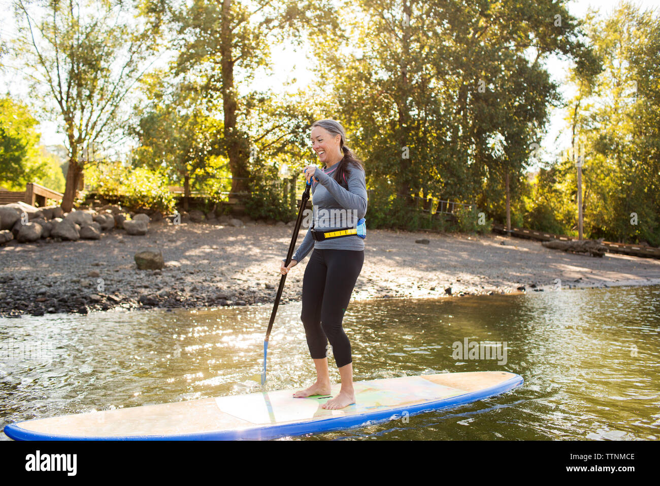 Die ganze Länge der lächelnde Frau paddleboarding auf dem Fluss Stockfoto