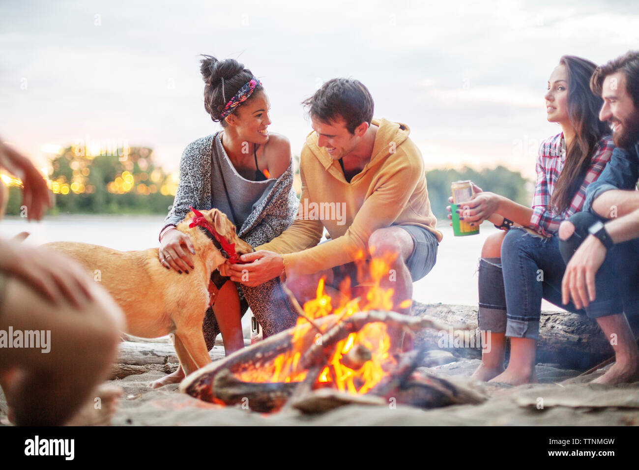 Gerne Freunde mit Hund von Lagerfeuer gegen River Stockfoto