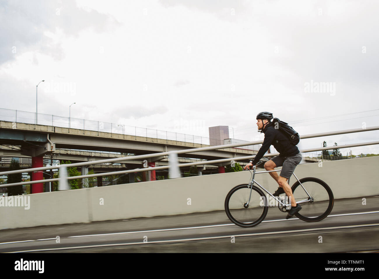 Seitenansicht der männlichen Pendler mit Rucksack, Fahrrad auf Brücke gegen Sky Stockfoto