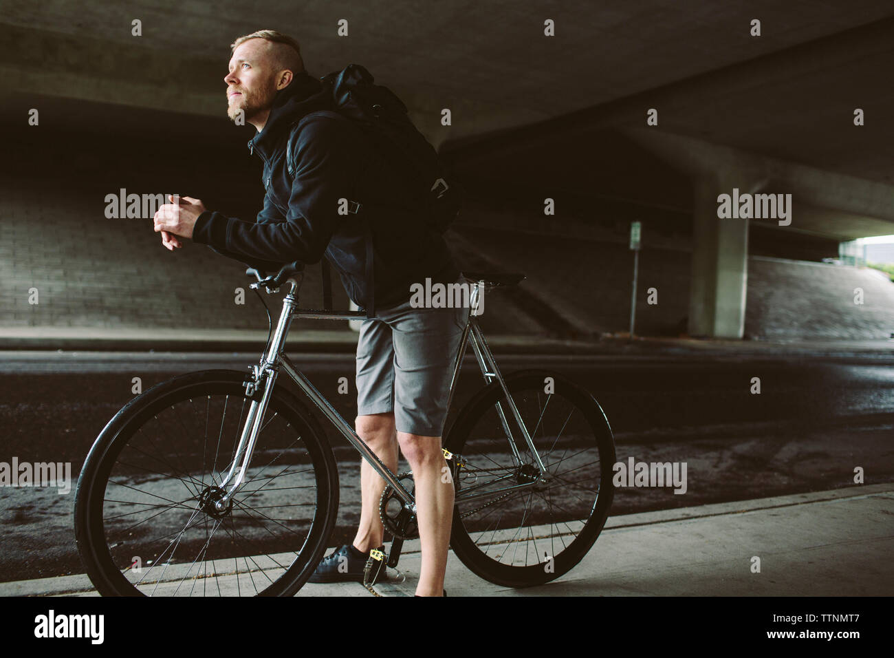 Männliche Pendler mit Fahrrad weg schauen beim Stehen auf Brücke Stockfoto