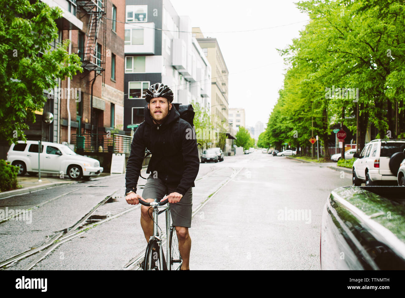 Männliche Pendler Reiten Fahrrad auf nasser Straße gegen Sky Stockfoto