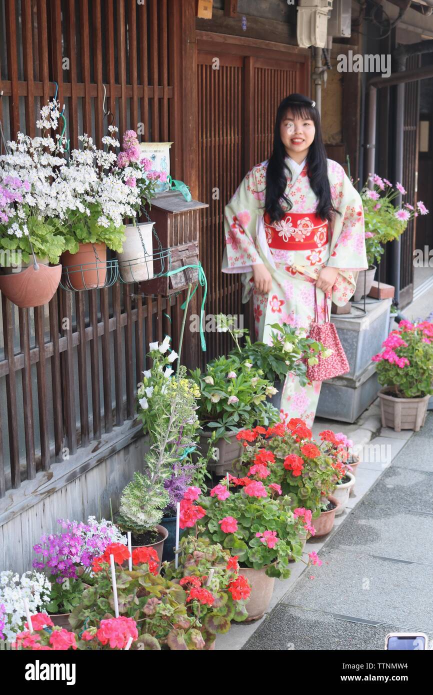 Japanische Mädchen im Kimono vor traditionellen hölzernen Lattenrost Haus mit vielen Töpfe Blumen um Sie herum Stockfoto