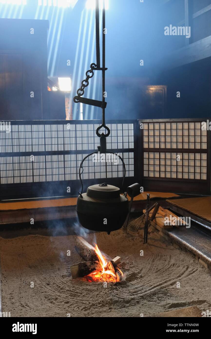 Traditionelle Japanische irori oder versunkenen hearth Anzeigen leuchtet Feuer mit schwarzem Gusseisen Wasserkocher darüber ausgesetzt, Bildschirme hinter sich und Licht, das in Stockfoto