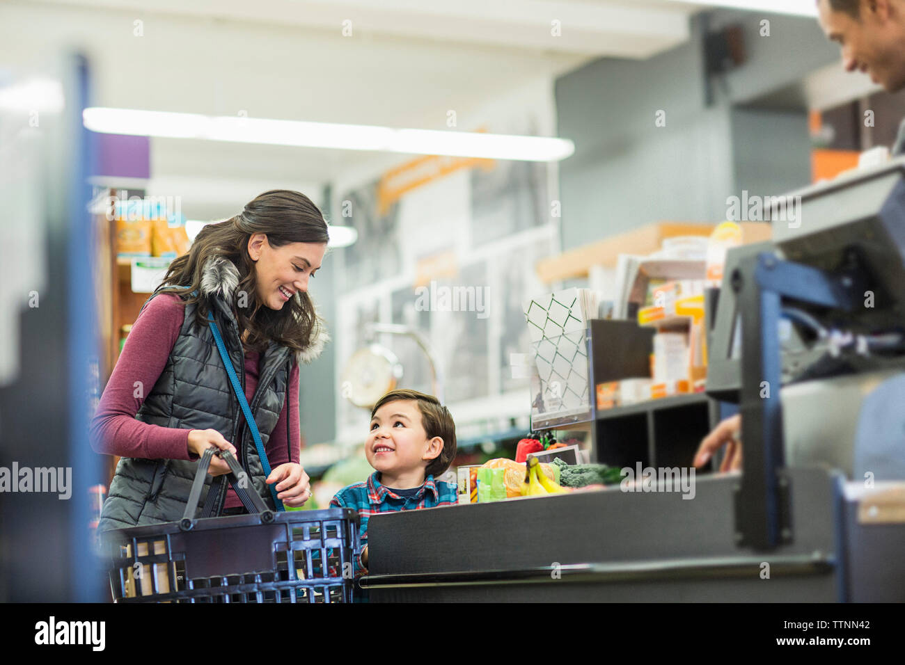 Lächelnde Frau mit Korb stehend mit Sohn durch die Kasse im Supermarkt Stockfoto