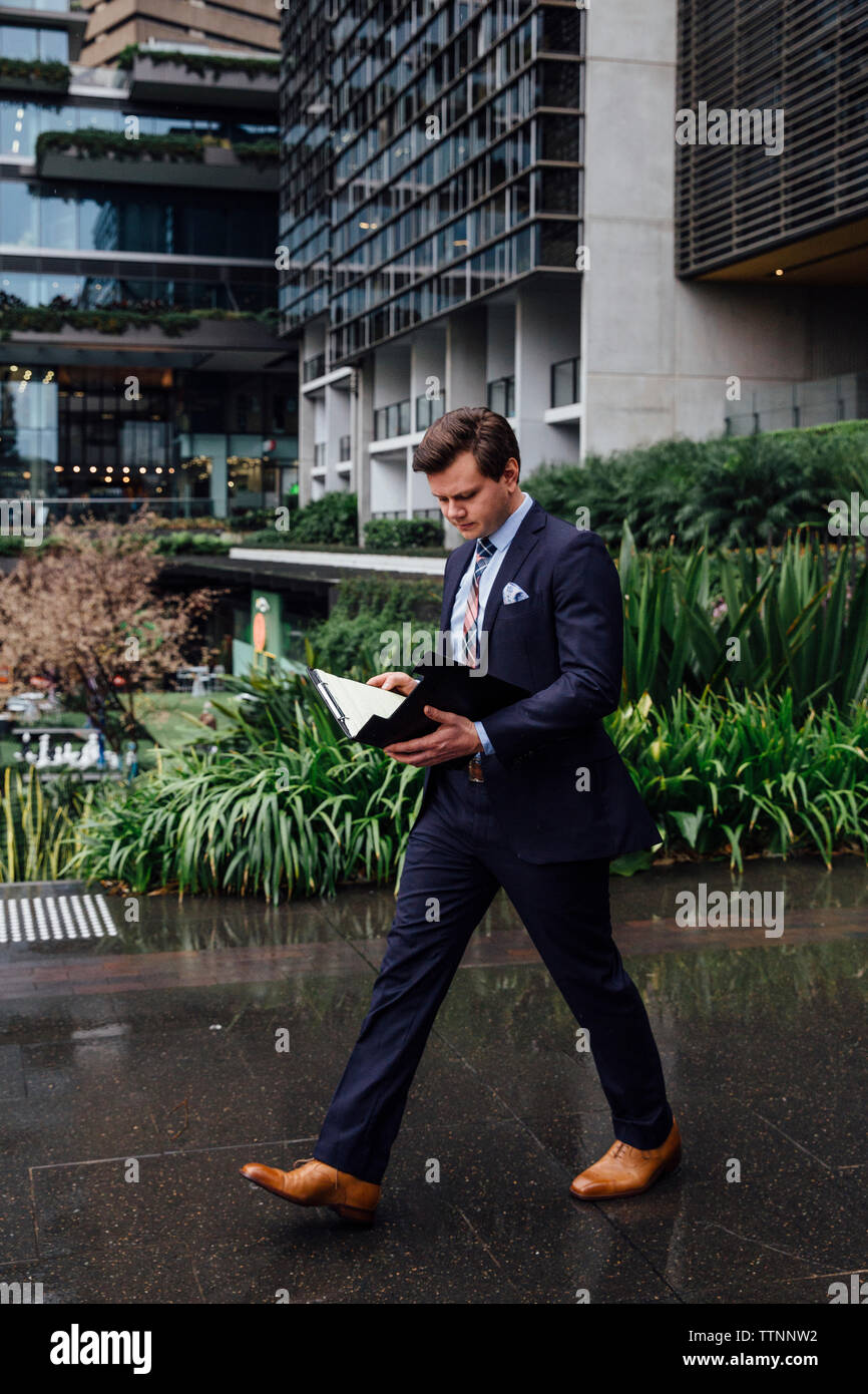 Geschäftsmann zu Fuß beim Lesen der Dokumente auf nassen Wanderweg in Stadt Stockfoto