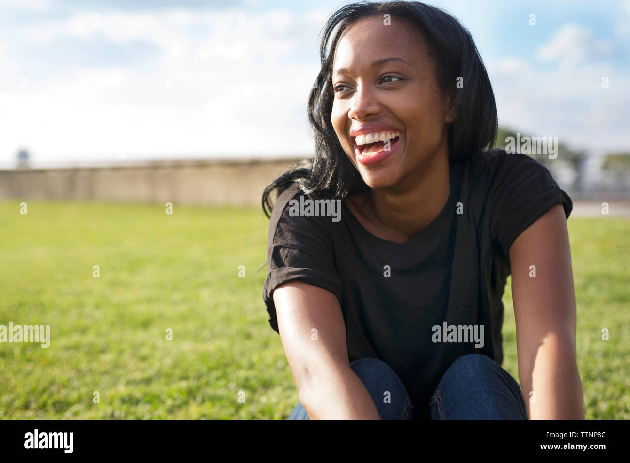 Fröhliche Frau sitzen auf dem Feld im Park Stockfoto