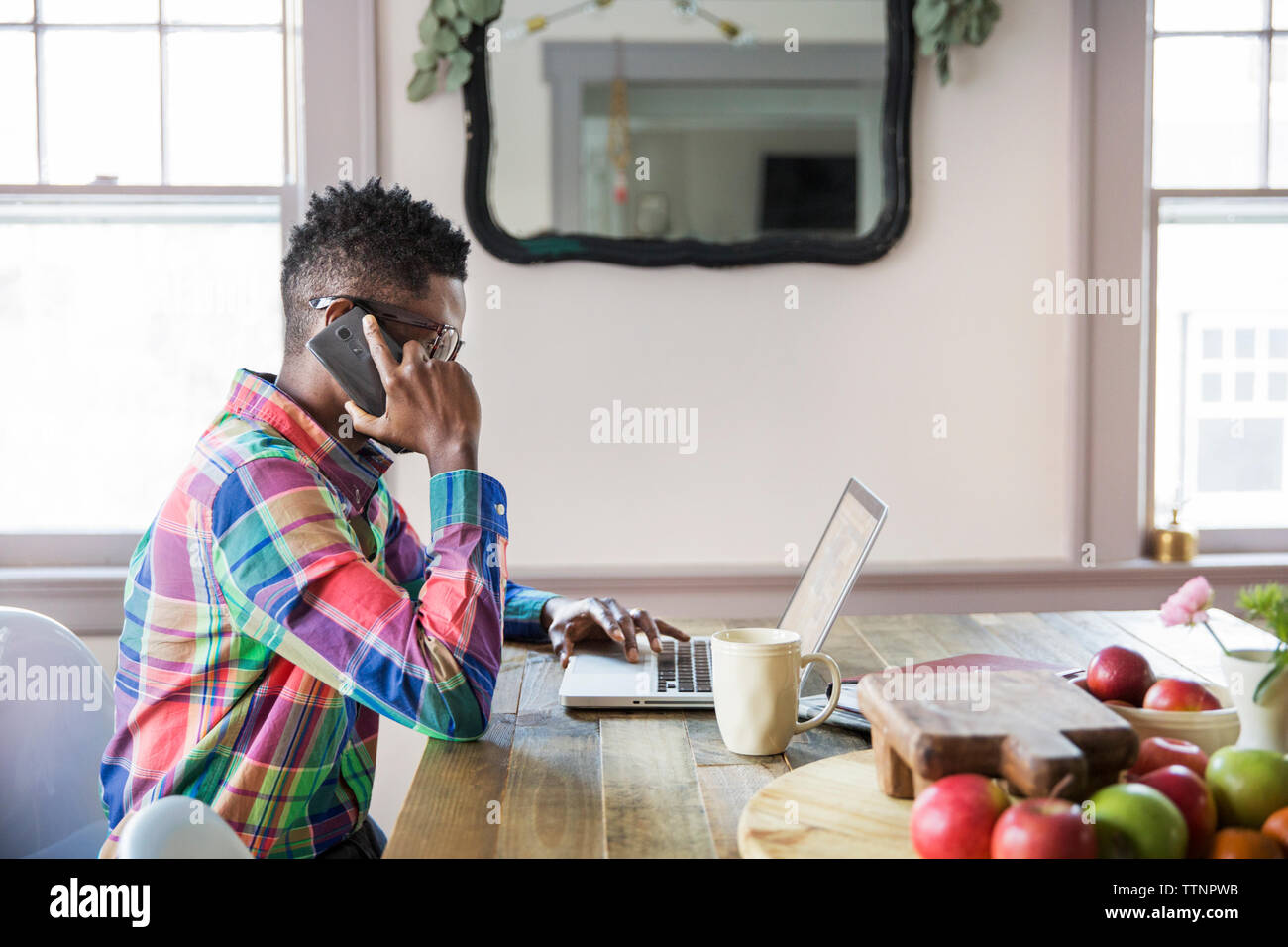 Seitenansicht des Geschäftsmannes Beantwortung smart phone, während auf dem Laptop zu Hause arbeiten Stockfoto