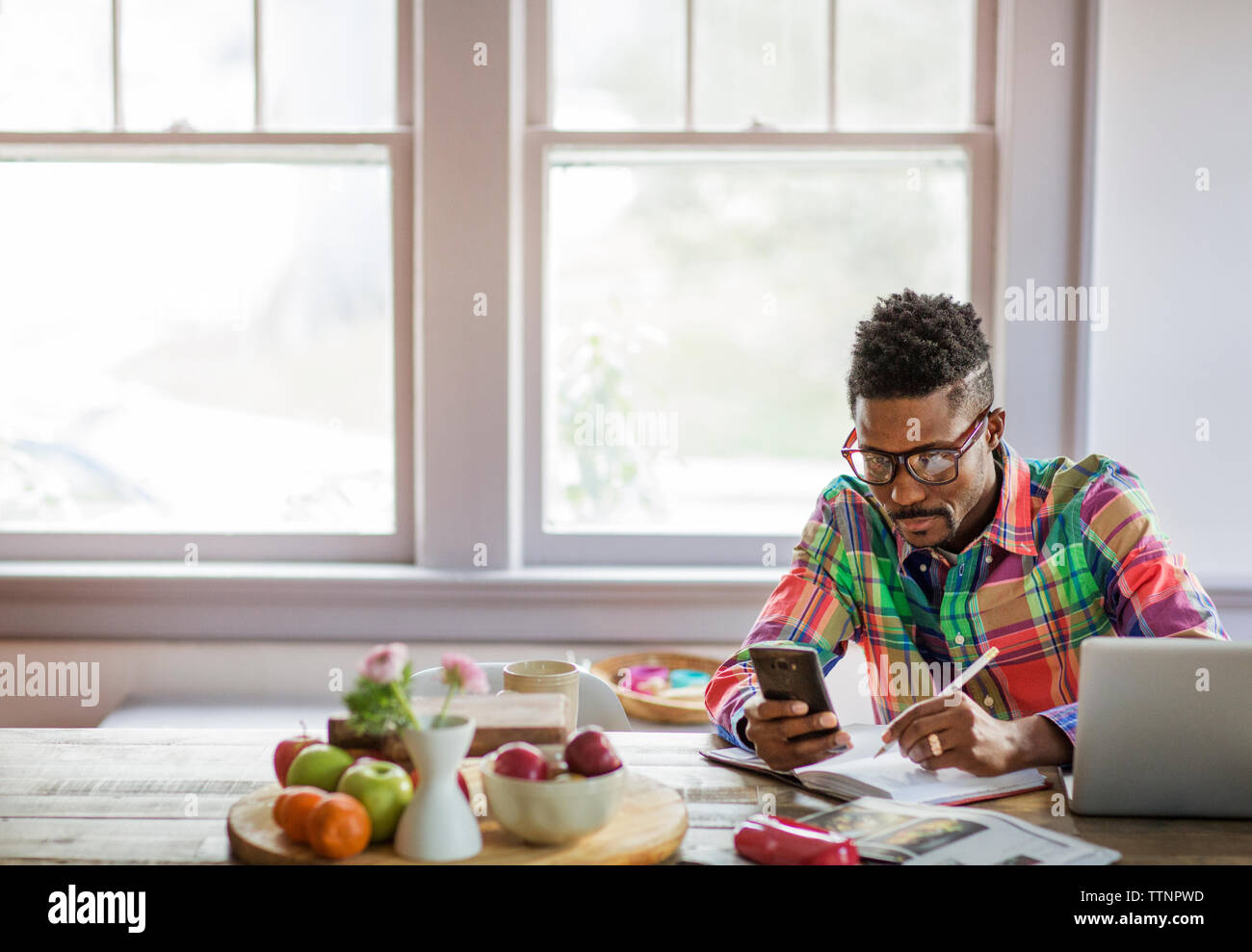 Mann mit Smart Phone beim Schreiben in Buch zu Hause Stockfoto
