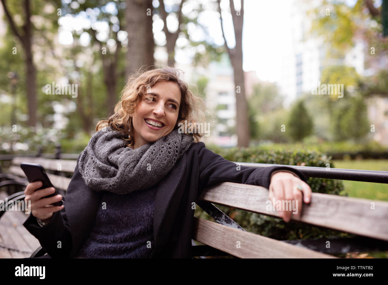 Frau mit Mobiltelefon, während auf der Bank im Park sitzen Stockfoto