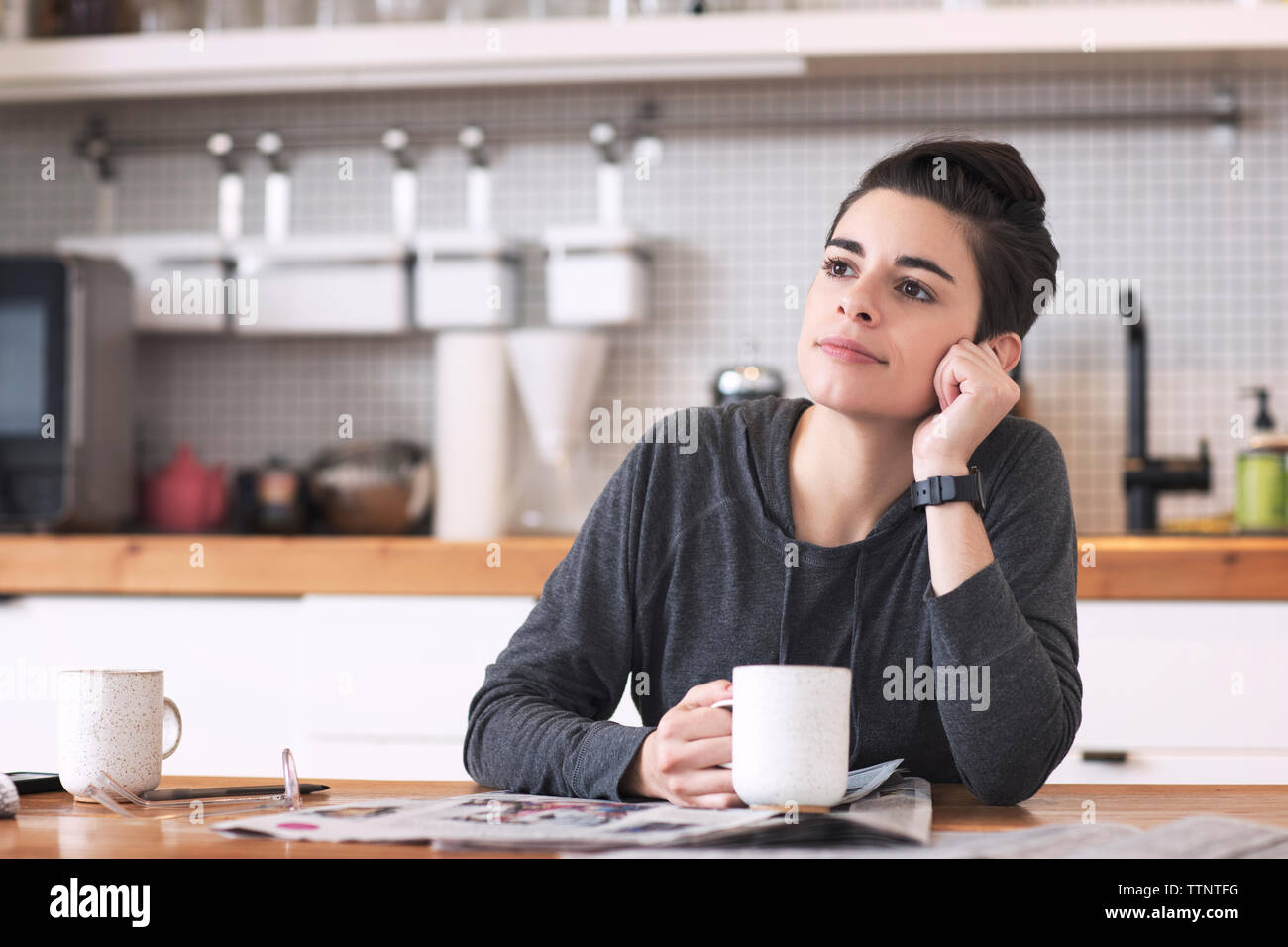 Frau mit Zeitungen und Kaffee Tasse weg schauen beim Sitzen am Esstisch Stockfoto