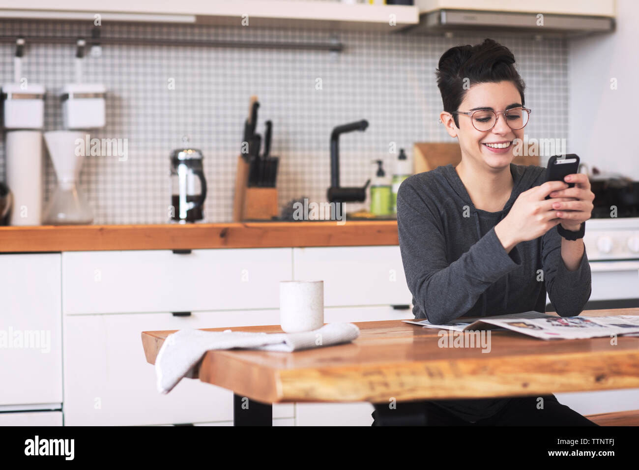 Glückliche Frau mittels Smart Phone am Esstisch in Stockfoto