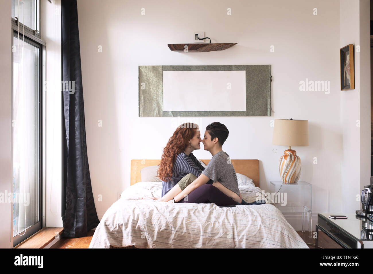 Seitenansicht der romantischen Lesben reiben Nasen beim Sitzen auf dem Bett Stockfoto