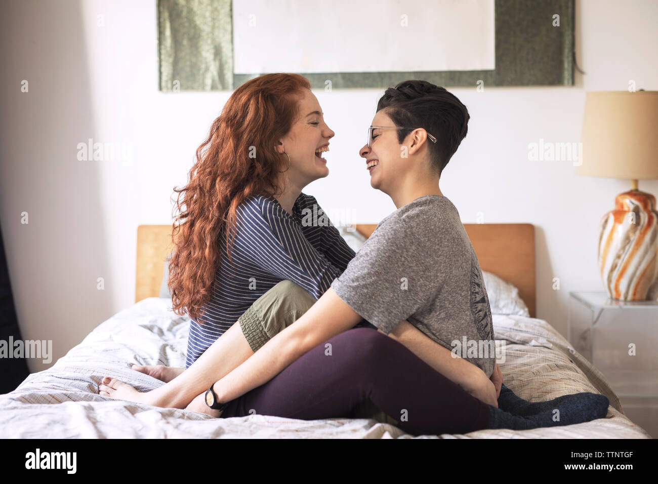 Seitenansicht des fröhlichen Lesben sich gegenseitig auf der Suche beim Sitzen auf dem Bett Stockfoto