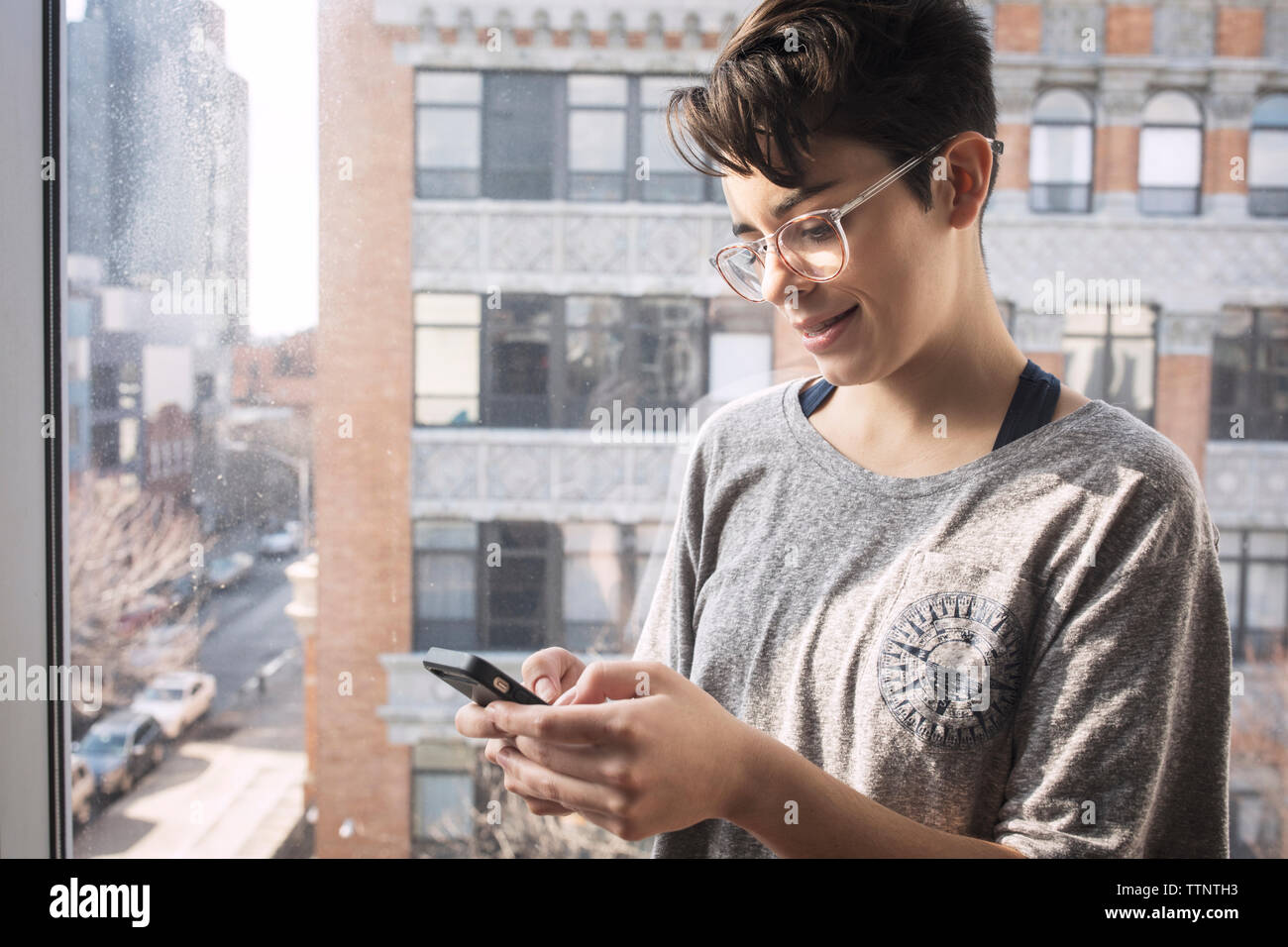 Frau in kurze Haare mit Handy beim Stehen durch Fenster Stockfoto
