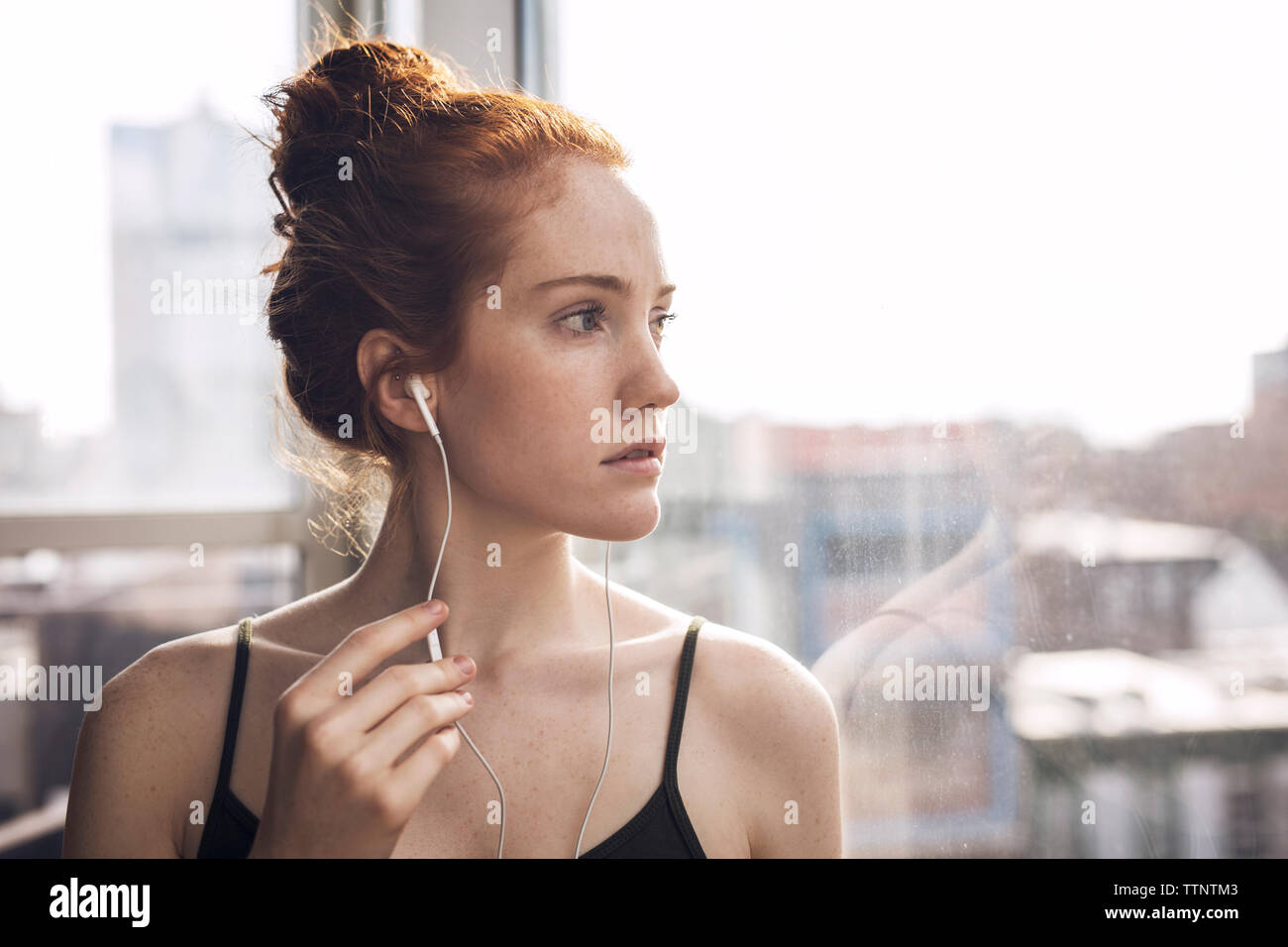 Close-up von nachdenklich Frau suchen durch das Fenster während der Wiedergabe von Musik zu Hause. Stockfoto